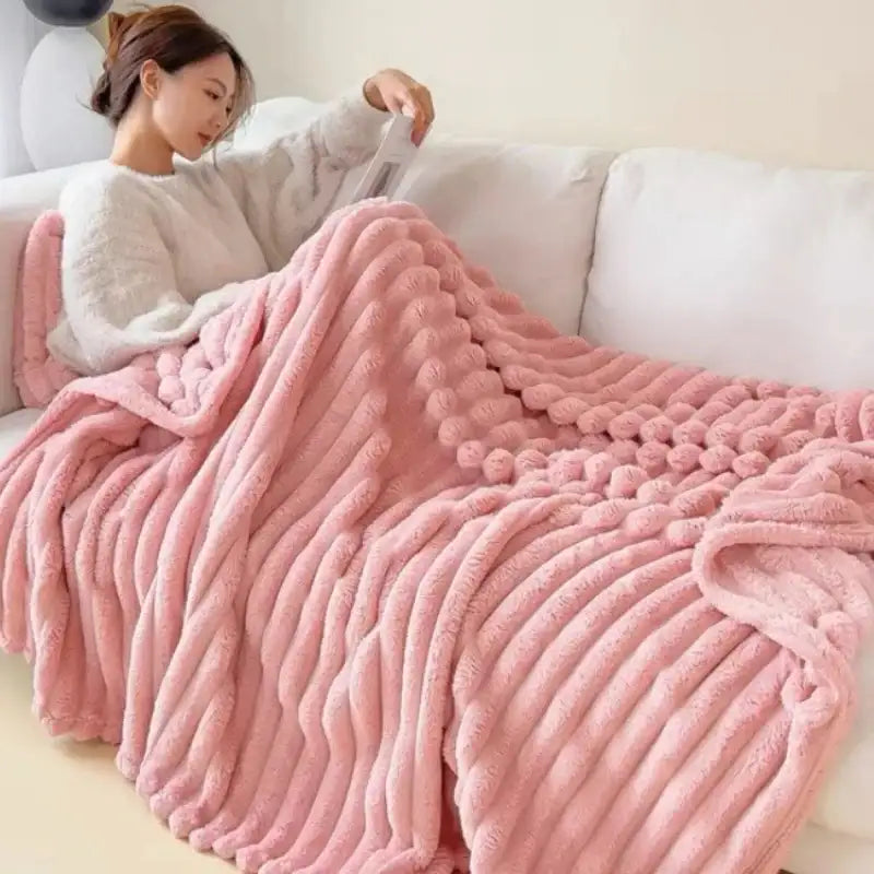 Couverture en peluche rose avec un motif texturé à côtes et des accents de pompons doux et moelleux.