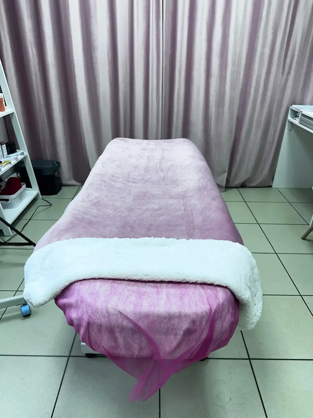 Une table de massage rose moelleuse drapée d'une couverture douce en polaire blanche.